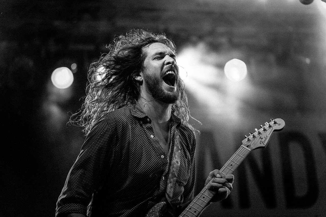 Singer shouting into the crowd while playing guitar under stage lights